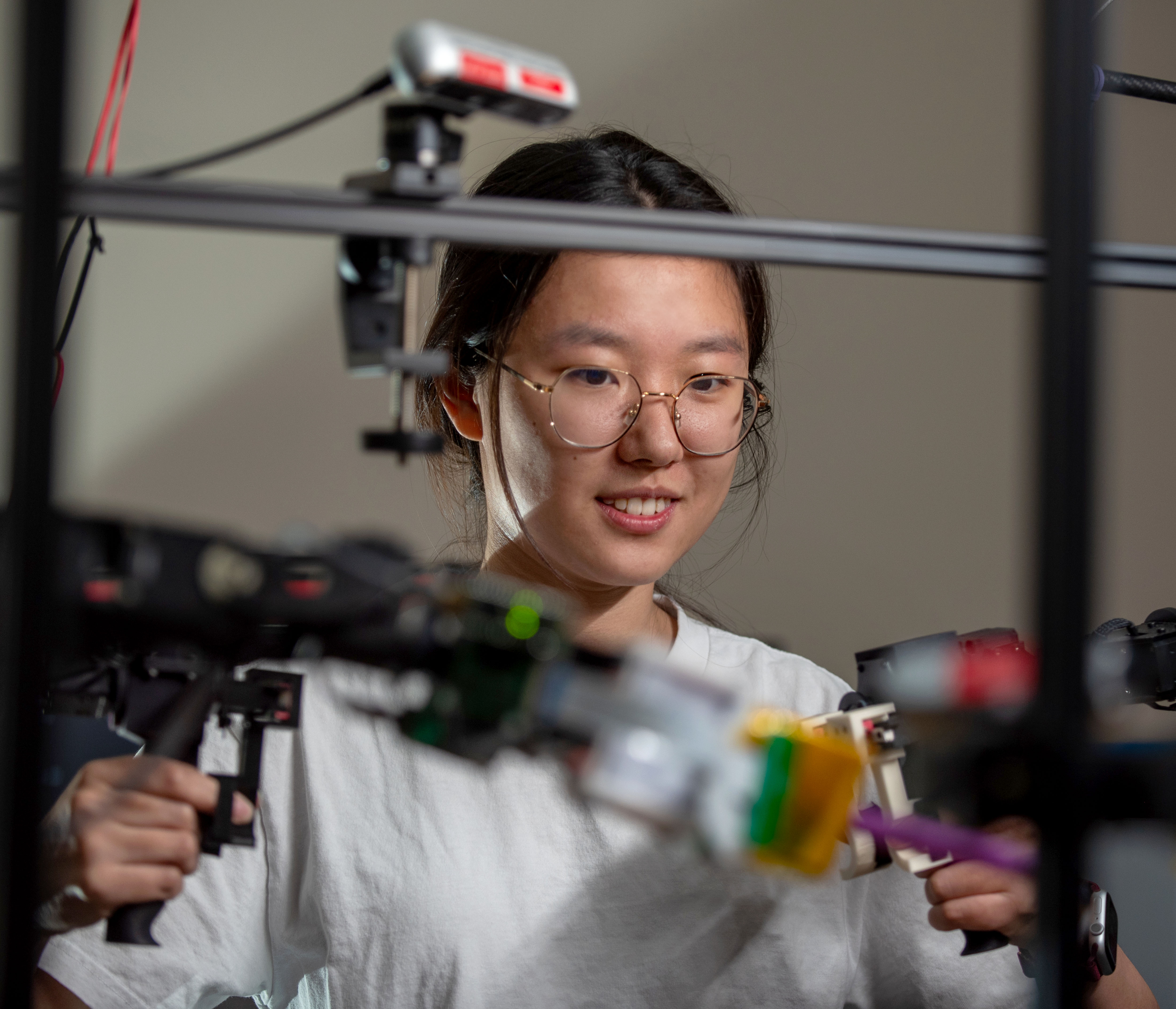 A young woman places her hands in a machine with handles and buttons as a robot mimics the movements.