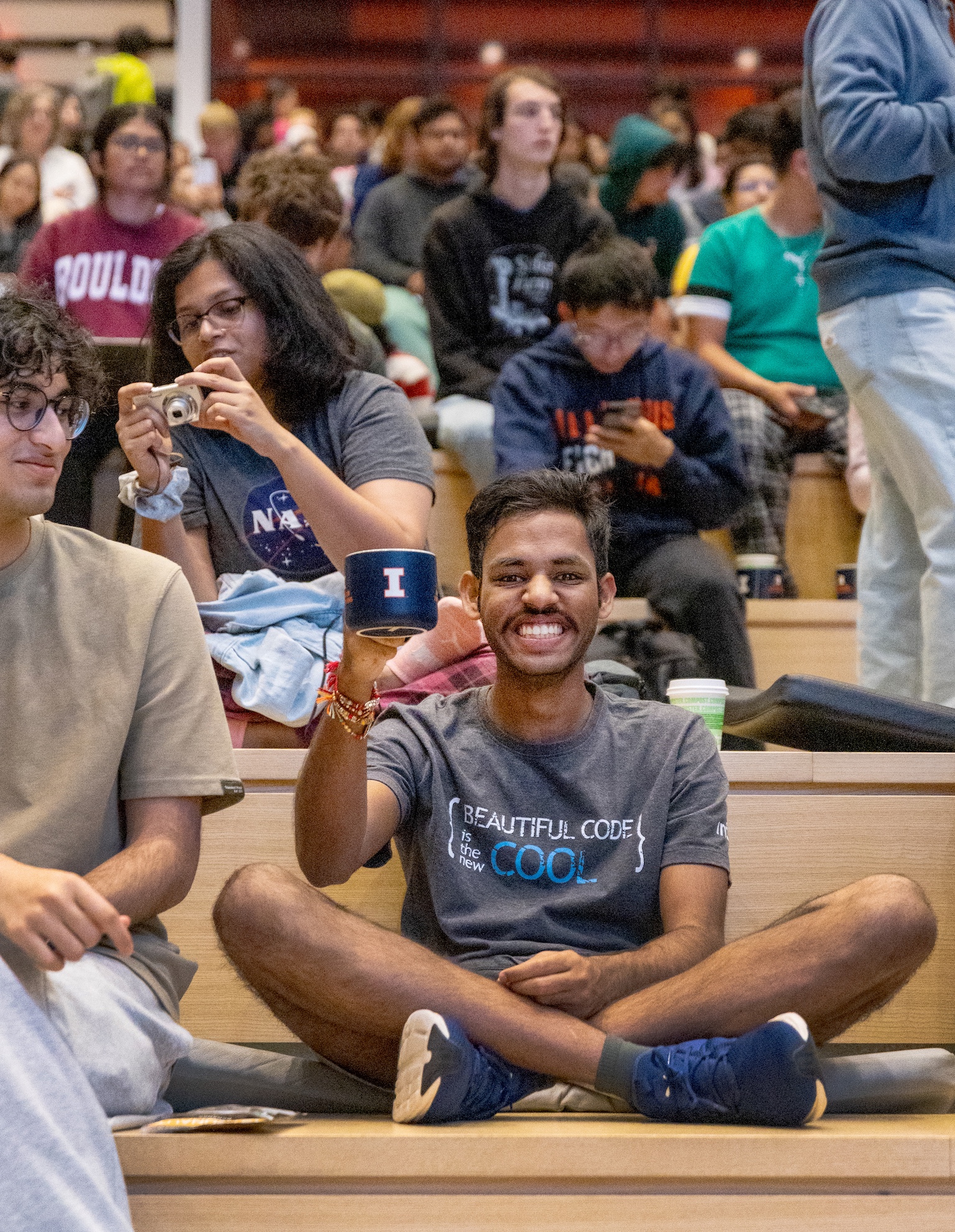 A student at the front of the crowd at the Carruthers Geocorona Observatory launch party holds up his Grainger Engineering coffee mug.