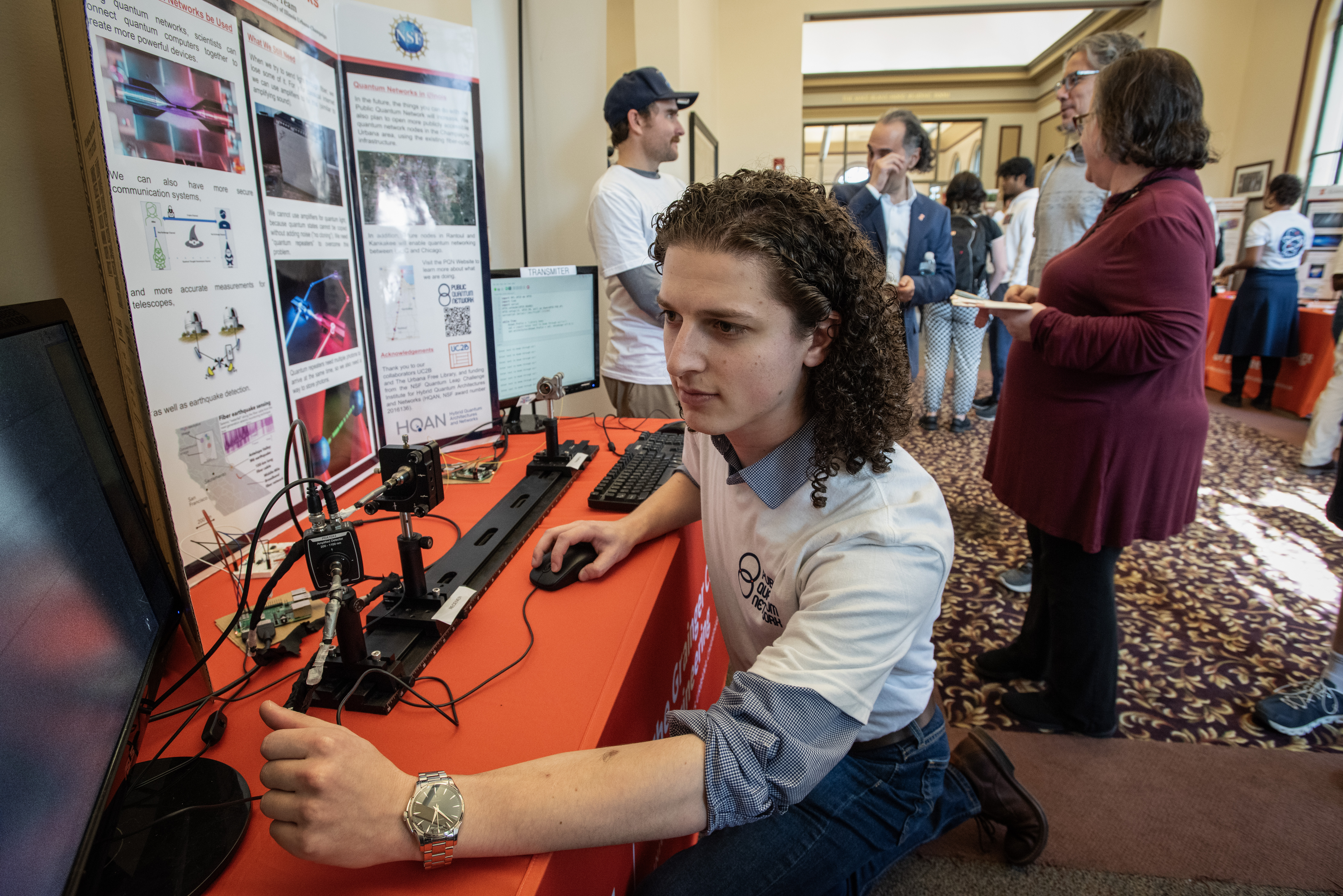 A man kneeling before a hub for the Public Quantum Network and looking at a computer.