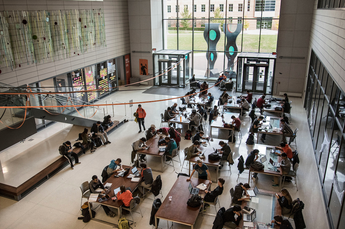An overhead shot of students at tables studying in the Electrical and Computer Engineering building, with large windows and an outdoor sculpture in the background.