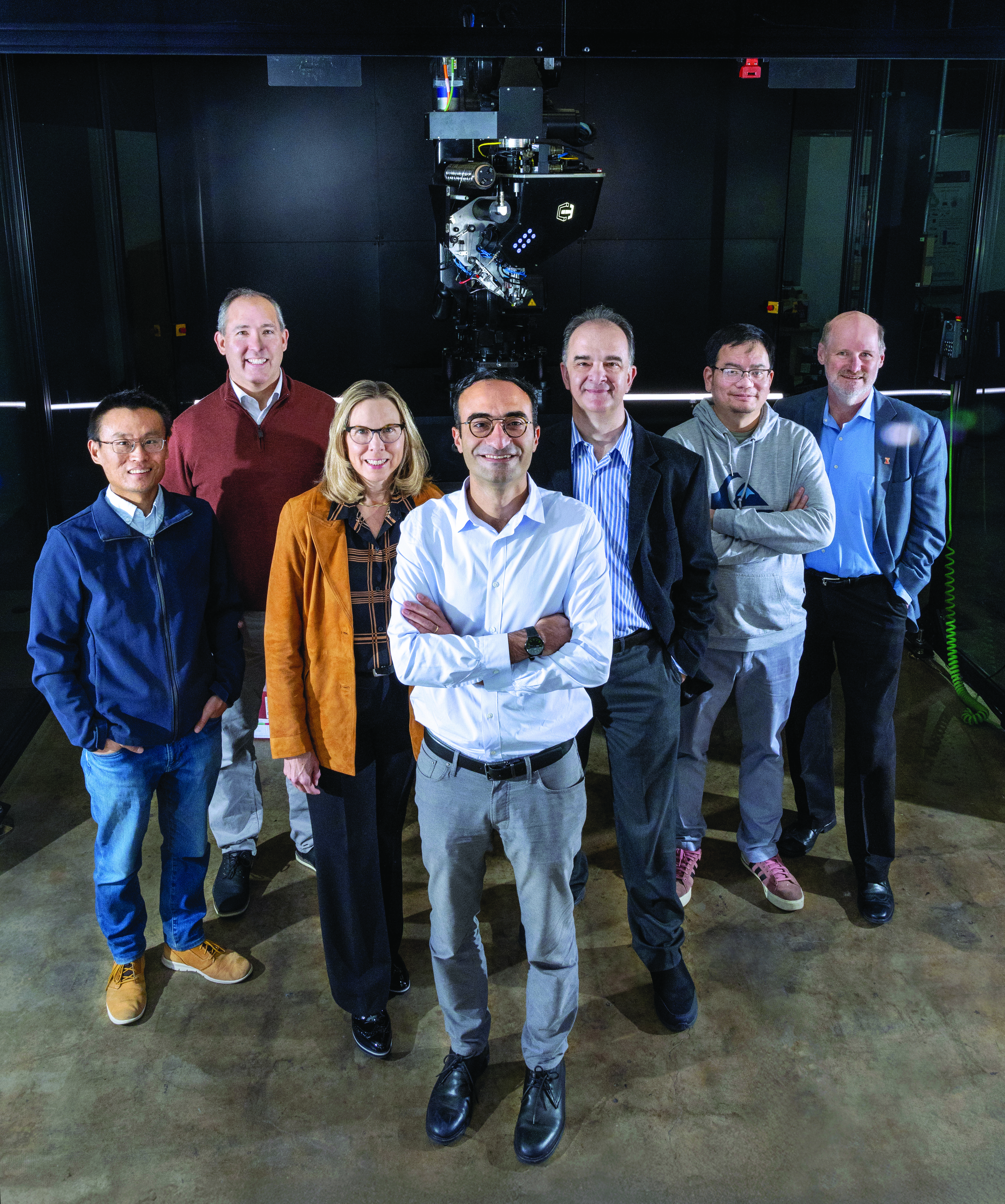 Researchers with the SpaceMaRS Center are L-R: Xin Ning, Jeff Bauer, Nancy Sottos, Sameh Tawfick, Ioannis Chasiotis, Huck Beng Chew and Philippe Geubelle. Not pictured is Jeff Moore. They were posing in front of the continuous fiber 3D printer at the Optical Physics Engineering Building (OPEL) in Champaign on Nov. 11, 2025.