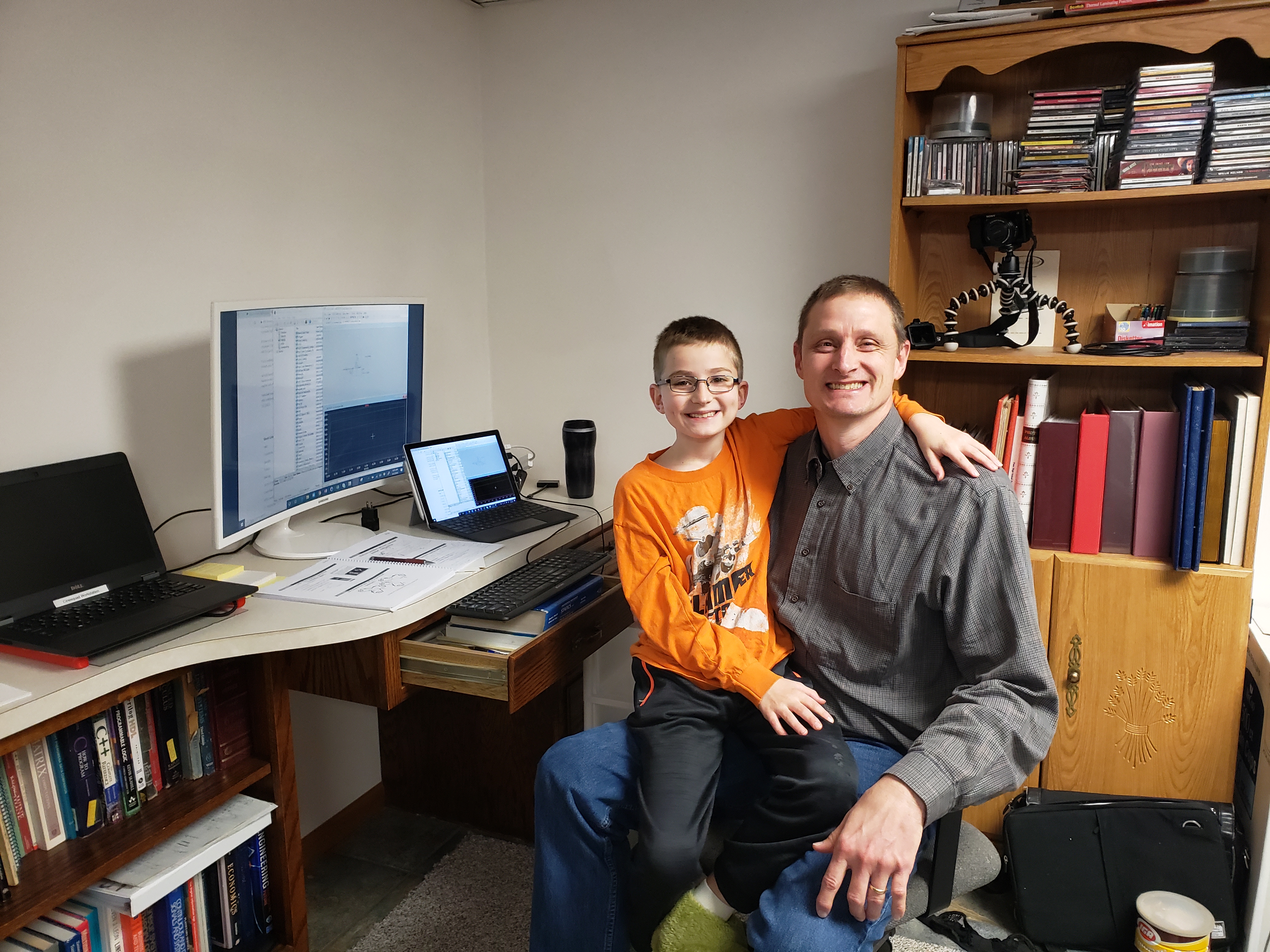 Chris Schmitz, an Electrical and Computer Engineering professor, pictured here with son, Ryan, balances home and work duties as he sets up to teach his ECE 110, Intro to Electronics course from his basement office. Schmitz credits his teaching assistants and resources, like PrairieLearn, with making online migration go more smoothly. Still, &quot;I really miss the face-to-face interactions,&quot; Schmitz said of teaching students. (photo provided by Chris Schmitz)