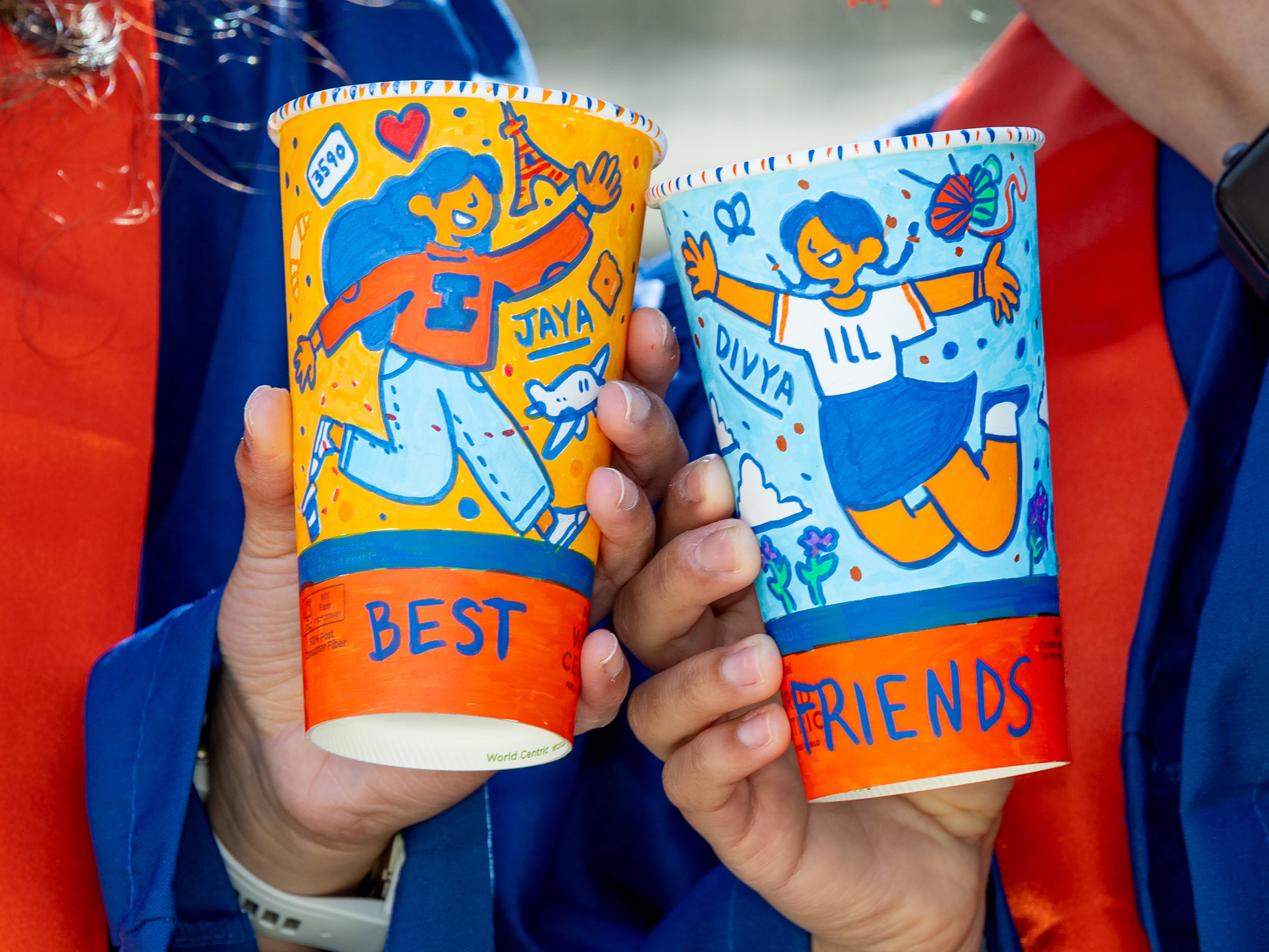 Divya and Jaya holding their colorful Illinois "Best Friends" cups on the quad.