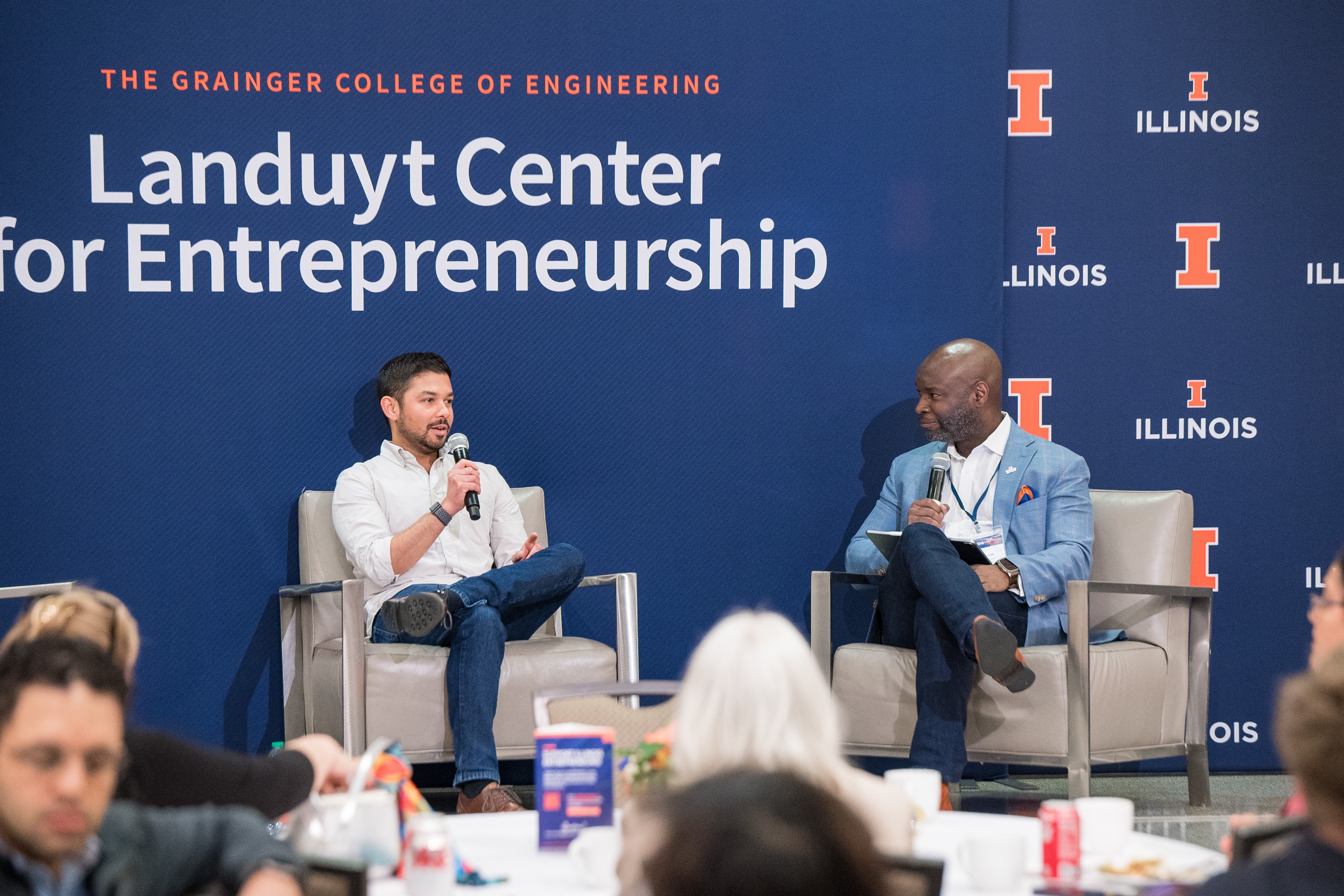 Devin Bhushan, left, and Gerald Wilson sit in chairs on a stage with background saying Landuyt Center for Entrepreneurship.