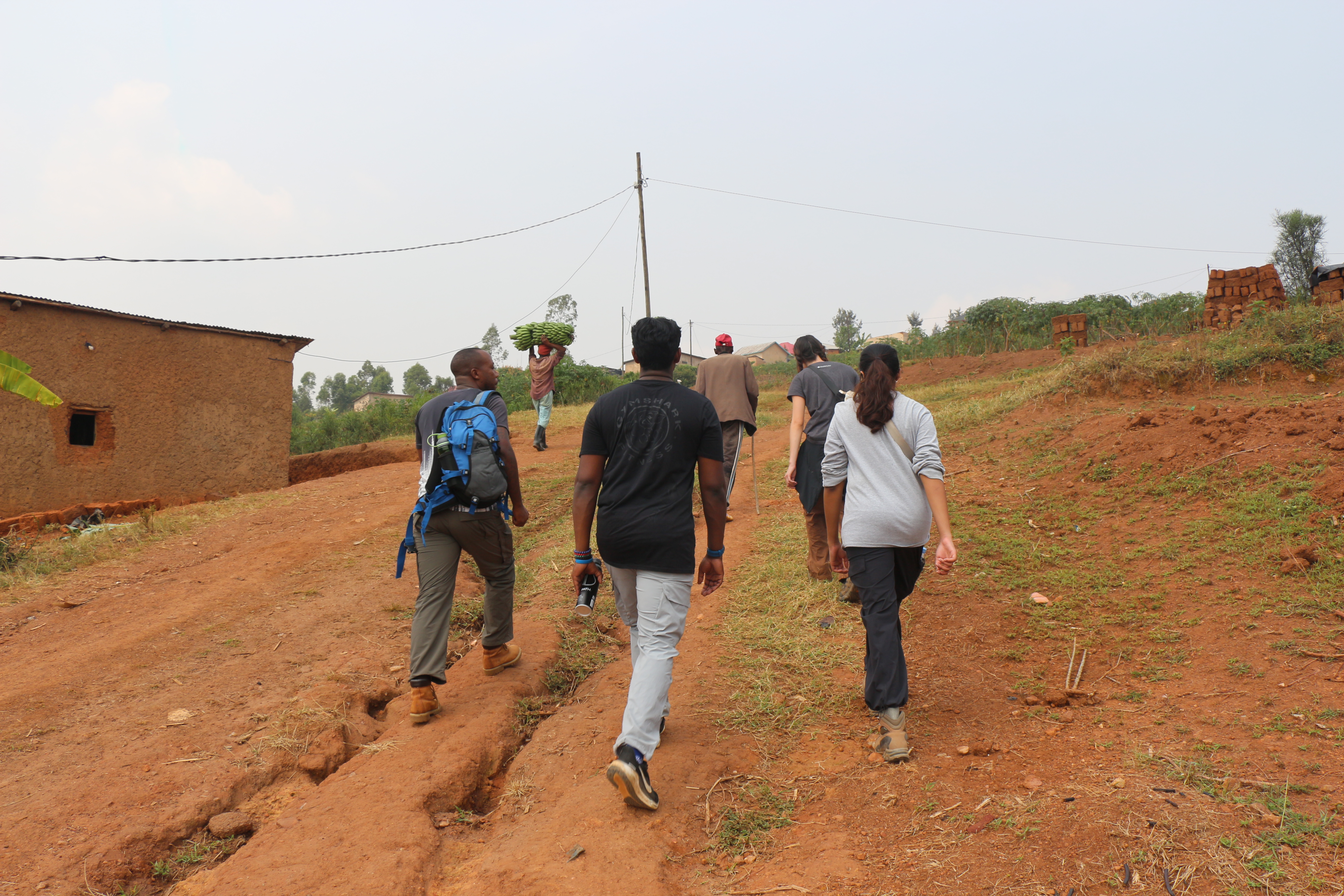 A group of residents and EWB volunteers walk up a steep hill in Rwanda.