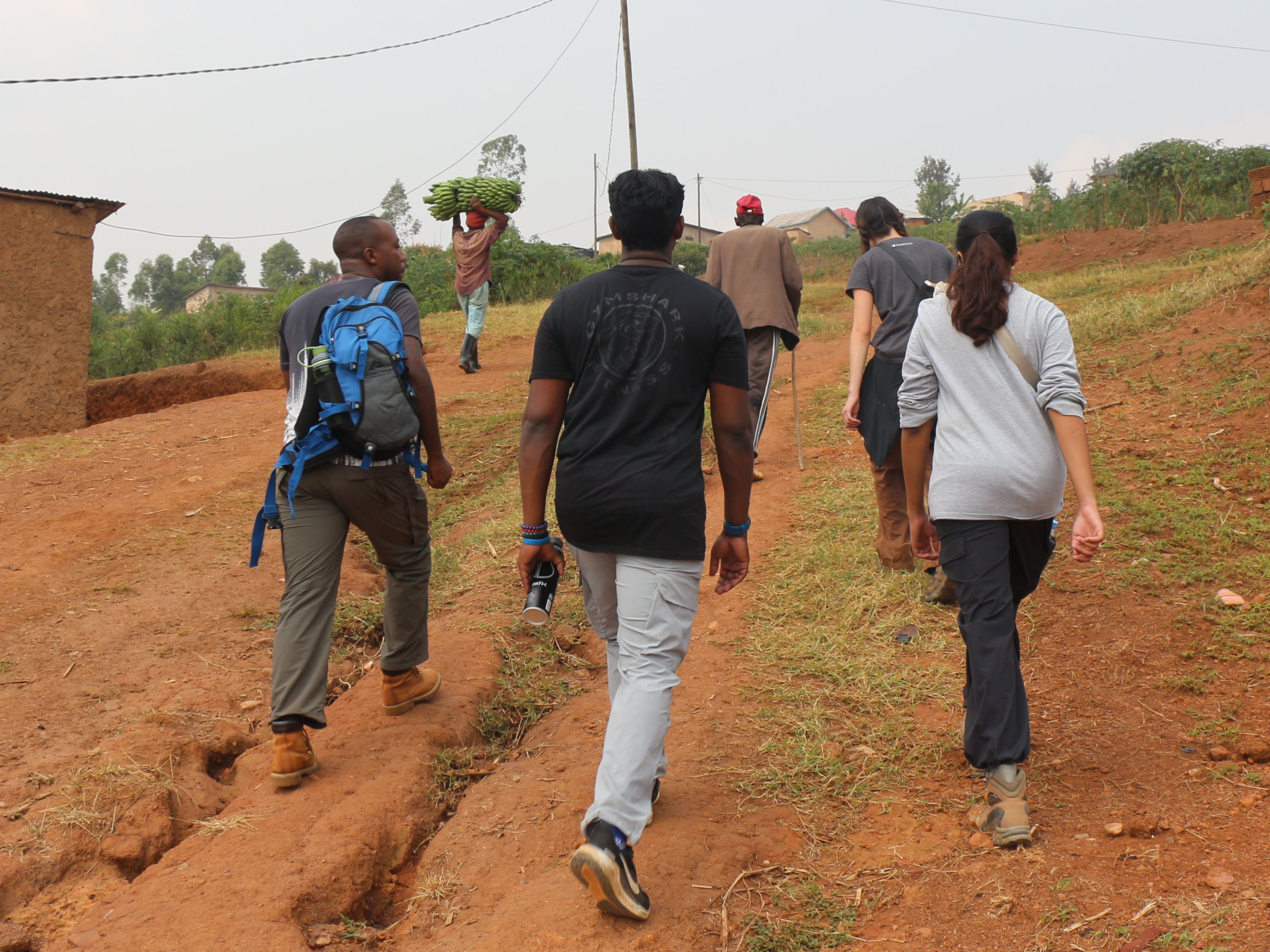 A group of residents and EWB volunteers walk up a steep hill in Rwanda.