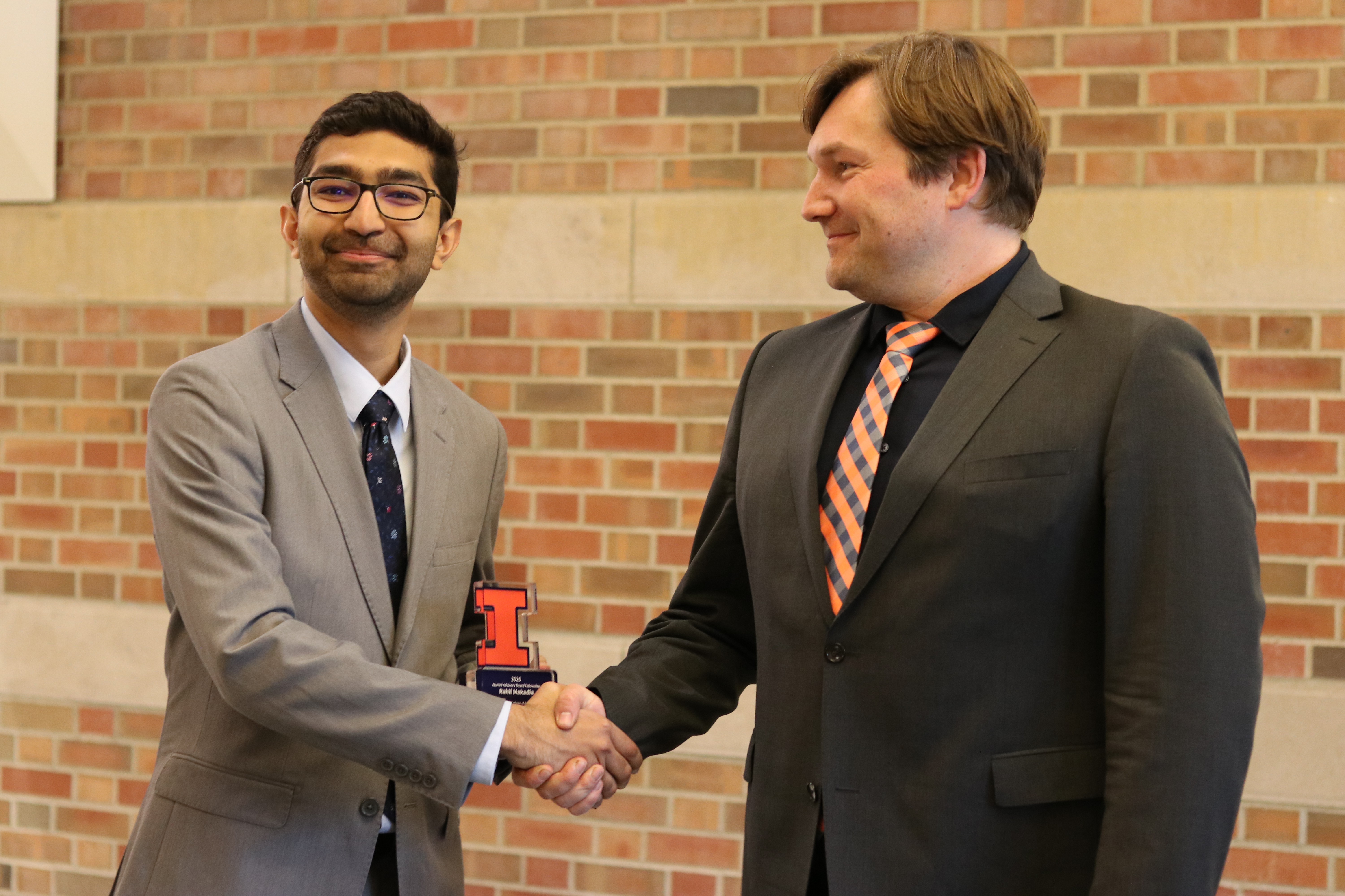 Two men shaking hands while one man holds an award