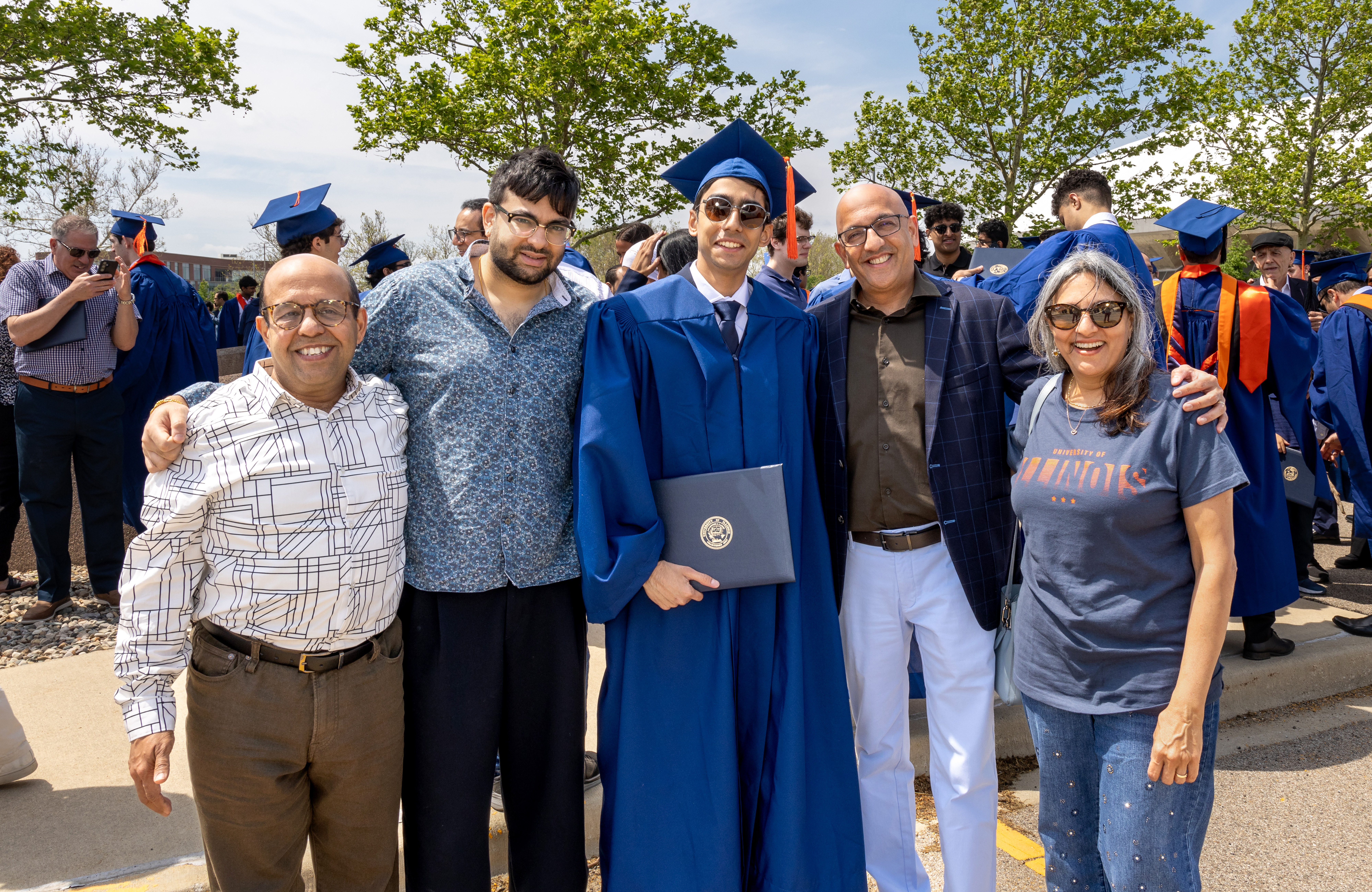 Nikhil Talwalkar, wearing sunglasses and dressed in a blue graduation cap and gown, poses with his family after Commencement ceremonies in 2026.