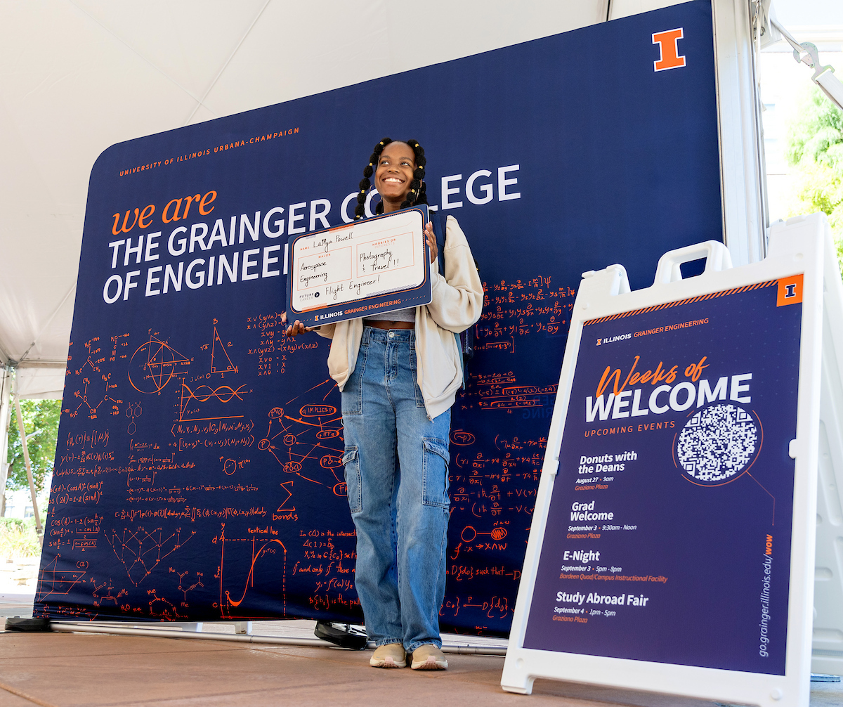 A student smiles for the camera in front of a backdrop during Grainger Engineering's First Day of Class Photo Op.