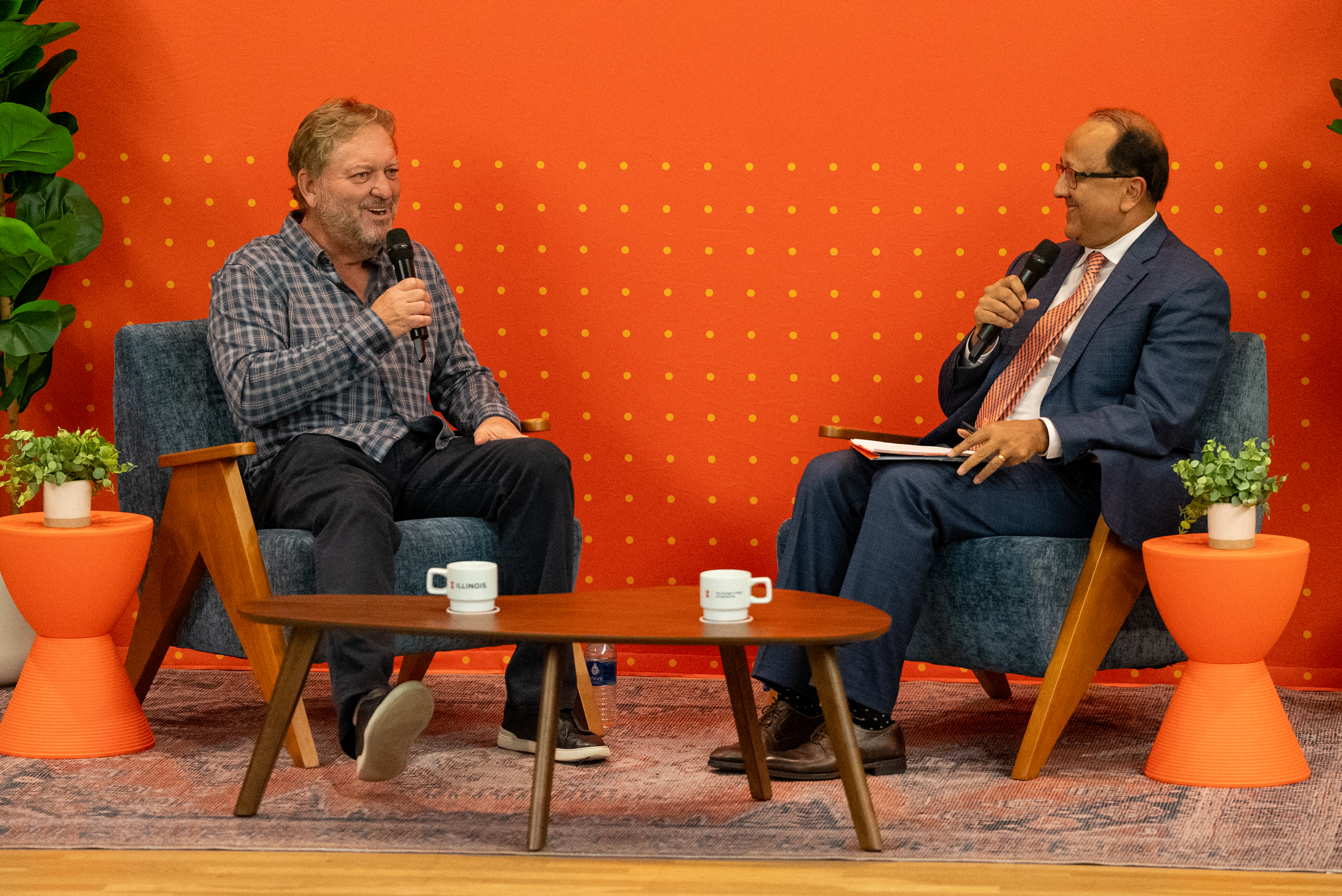 Dan Caruso and Rashid Bashir on a stage with a fireside chat setup holding microphones.