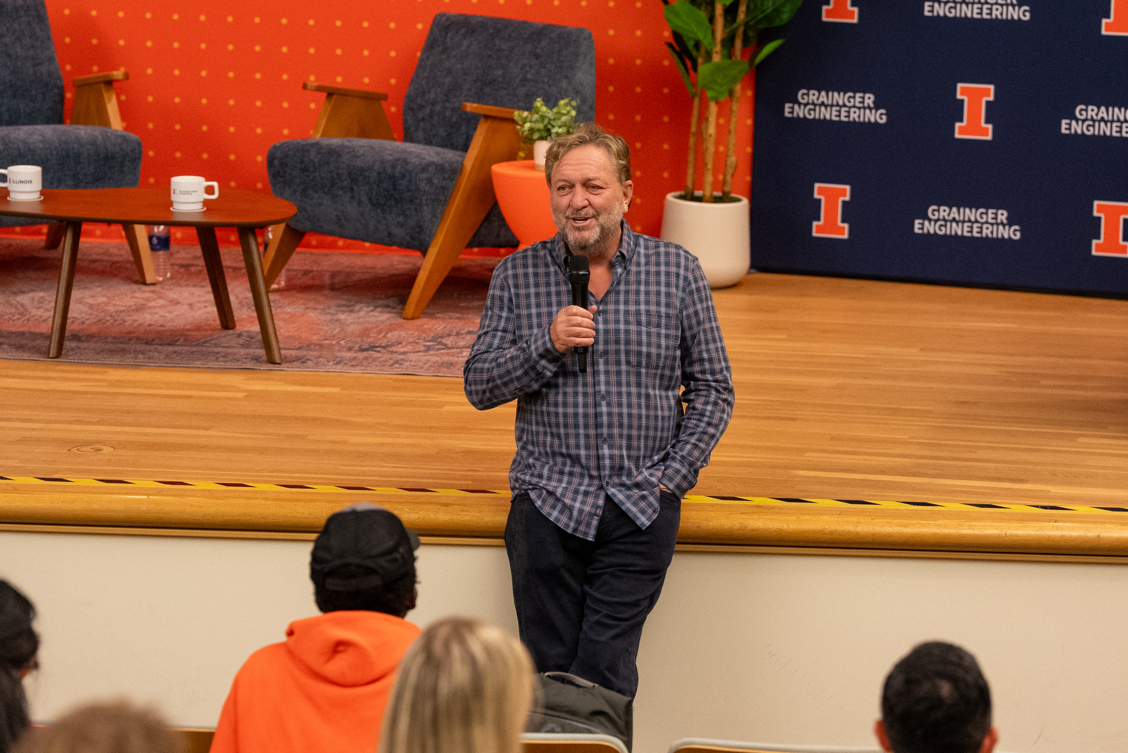 Dan Caruso in front of a stage with a microphone talking with students.