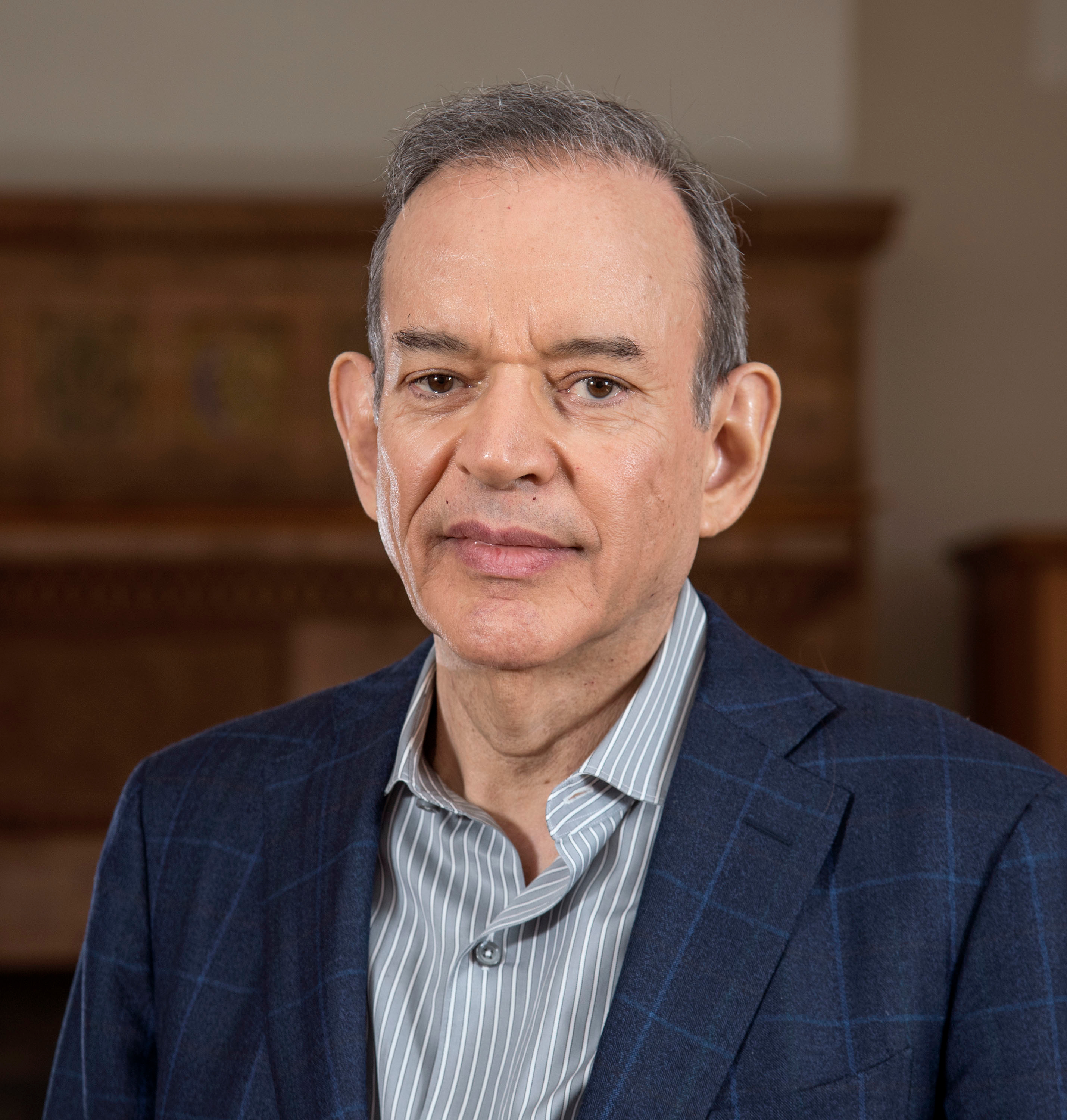 Headshot of a man in a blue suit and gray striped button down. 