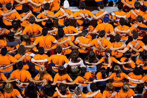 A sea of people wearing matching orange t-shirts with their arms on each others shoulders. 