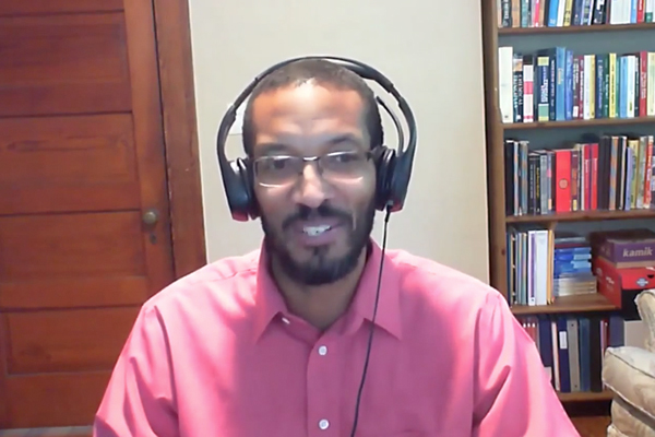 A man wearing headphones and a pink button down looking at the camera for a video call.