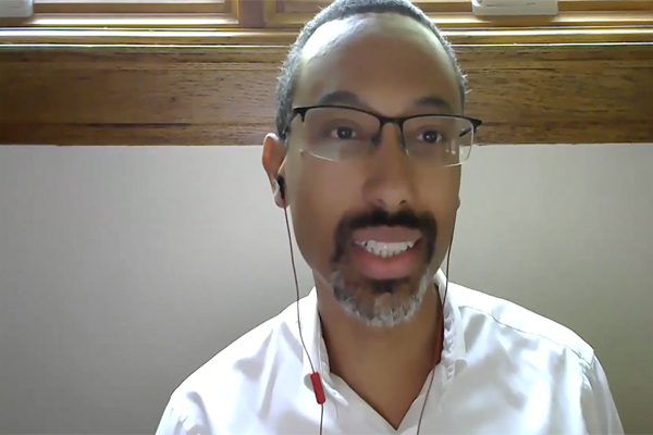 A man wearing earbuds and a white button down shirt looking at the camera for a video call.