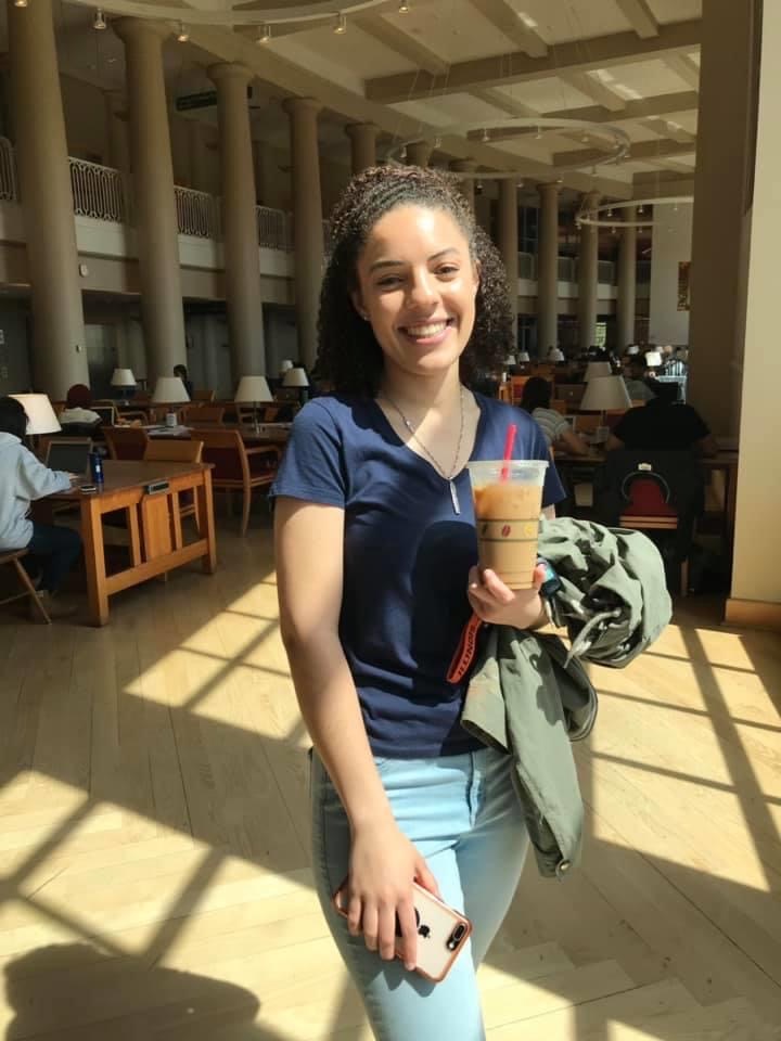 Caitlyn Person standing with a coffee smiling in the Grainger Engineering Library