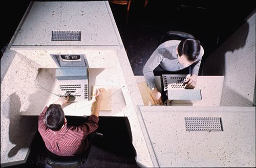 Aerial photograph of two men working on PLATO in separate cubicles
