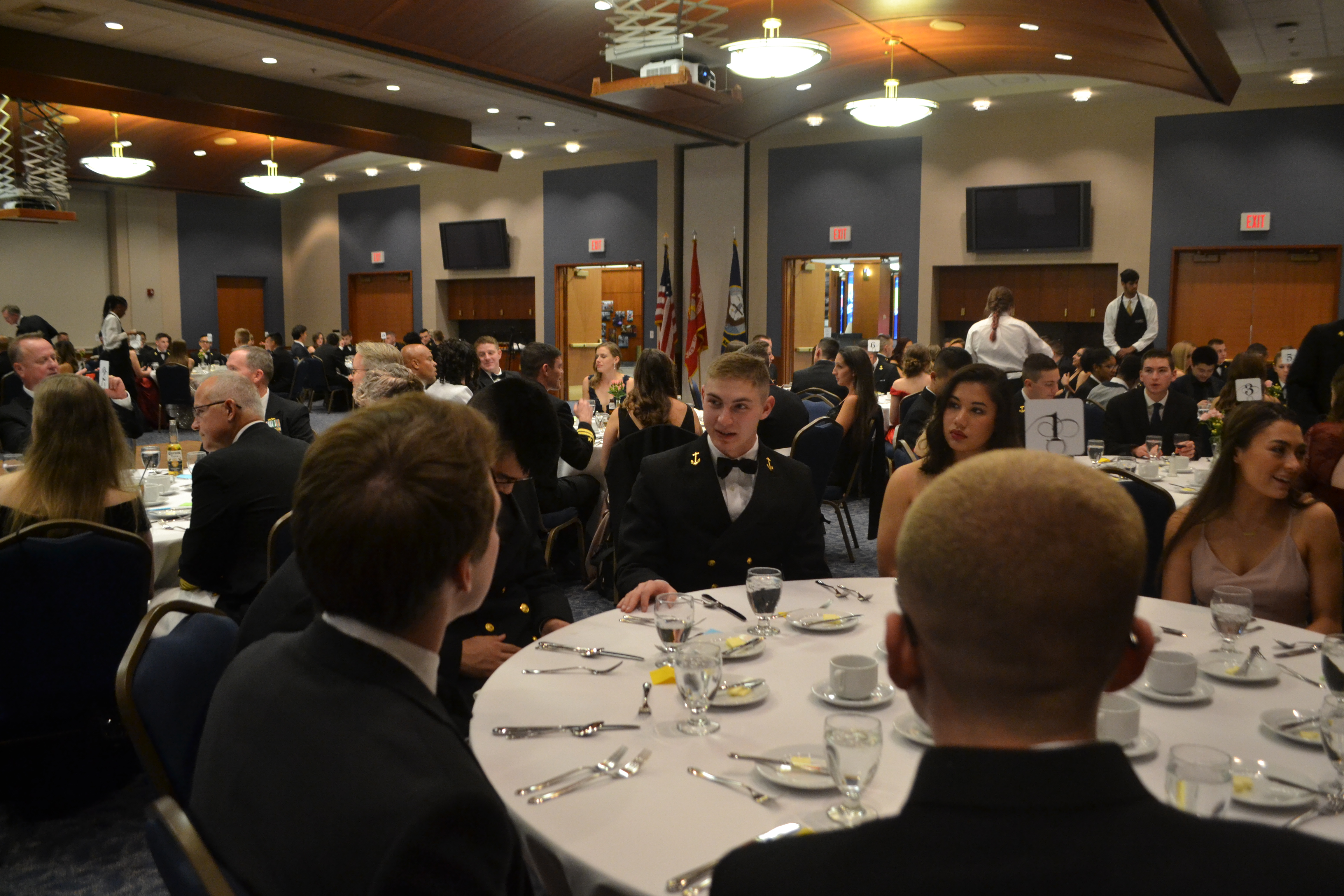 A group of students in military formal wear sit around large tables