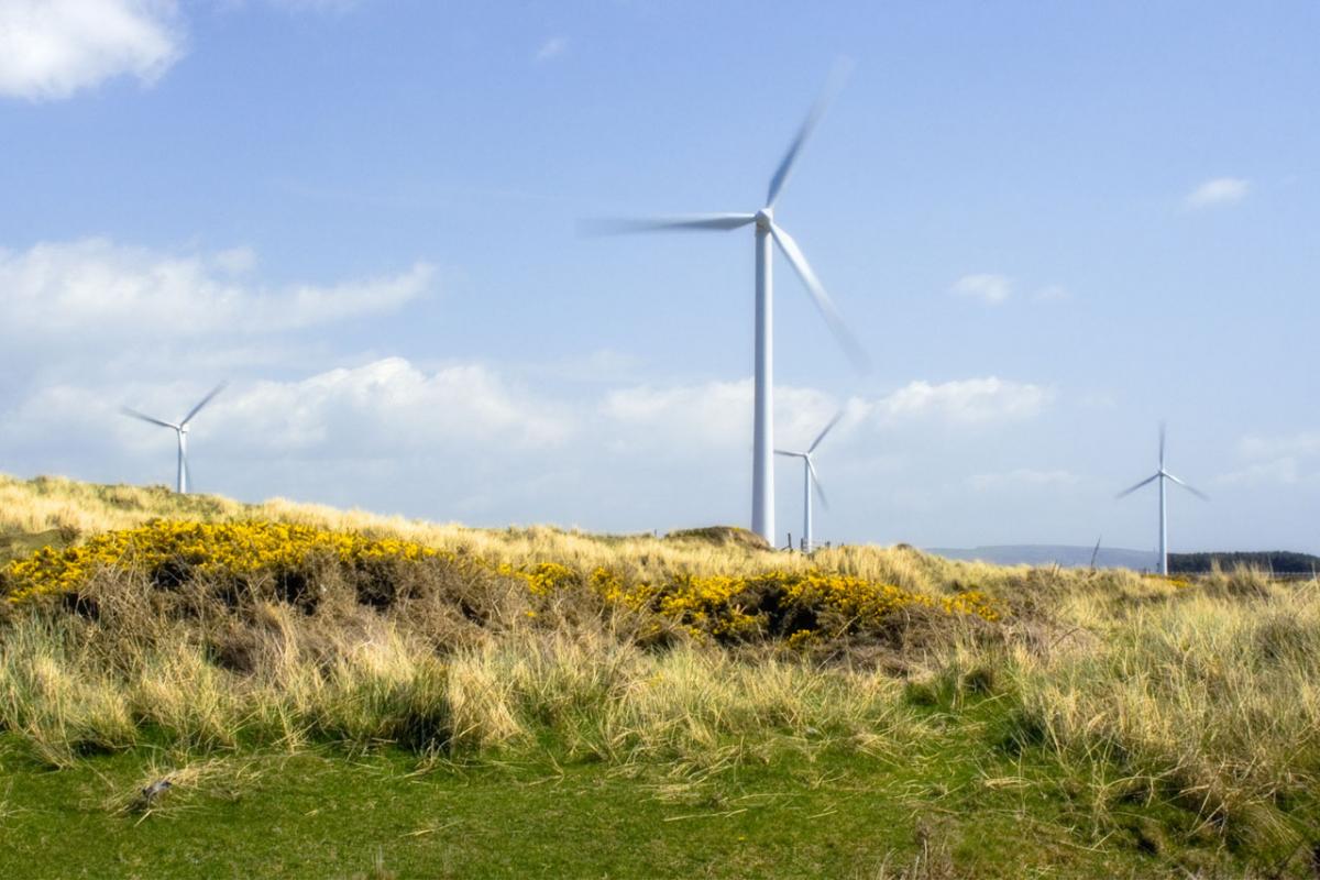 A white windmill in a grassy field with a cloudy blue sky in the background. 