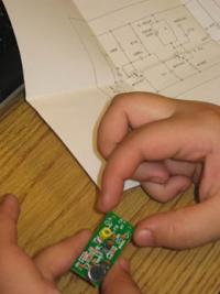 A camper checks the FM circuit she is soldering against the schematic.