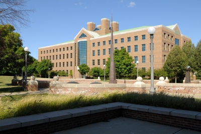 The Coordinated Science Laboratory, a tall brick building with many glass columns and windows, on a sunny spring day. 