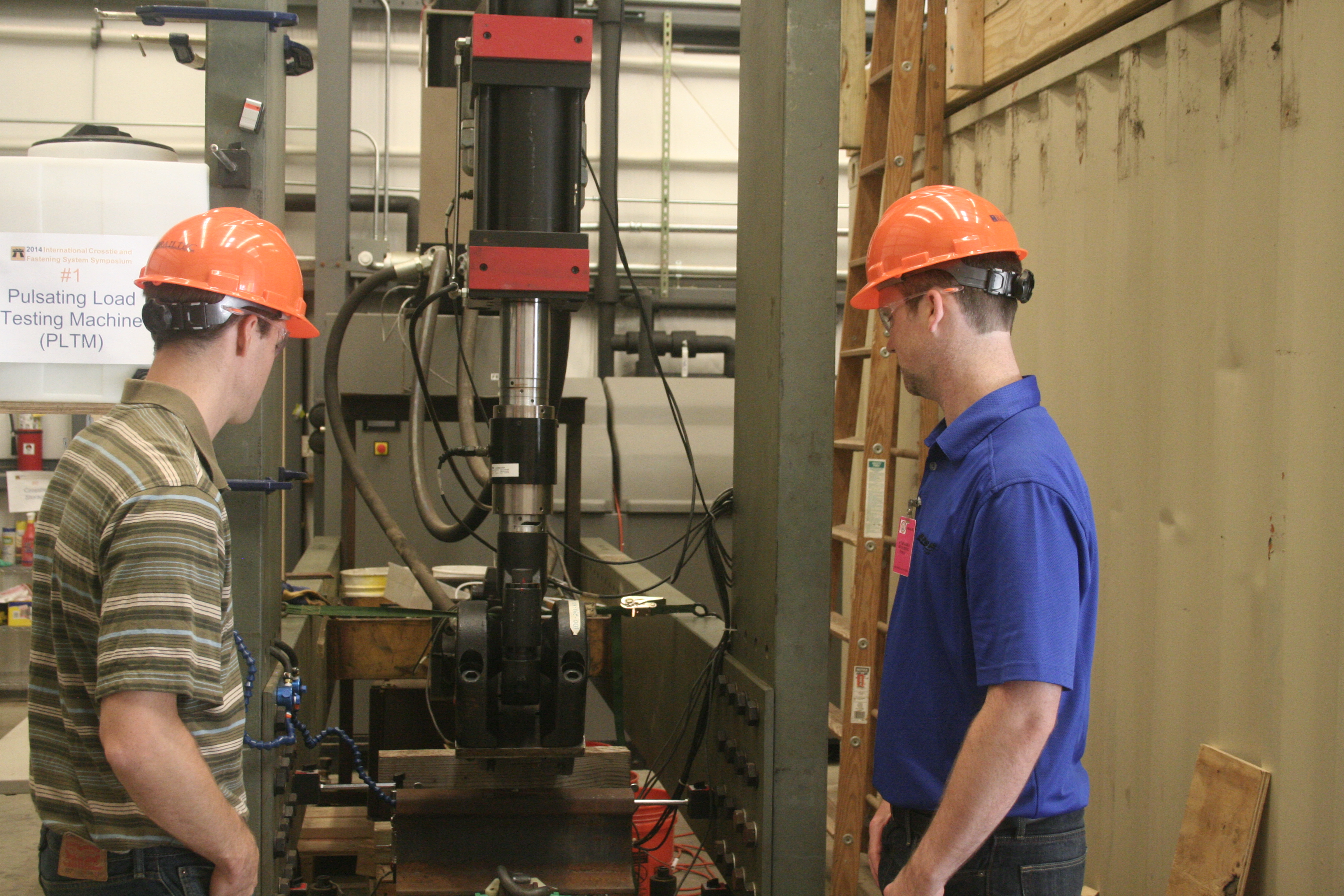 Marcus Dersch (left), research engineer, and Riley Edwards, research scientist and senior lecturer at RailTEC, exam the pulsating load test machine.