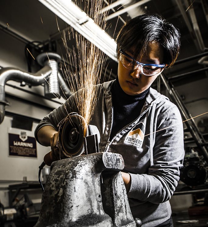 A female undergraduate mechanical science and engineering student uses a grinder at the Engineering Student Project Lab in the College of Engineering