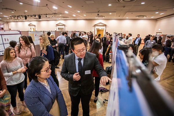 Groups of people gather around posters at the research symposium