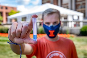 Student wearing a Block I mask holds up a test tube of blue liquid