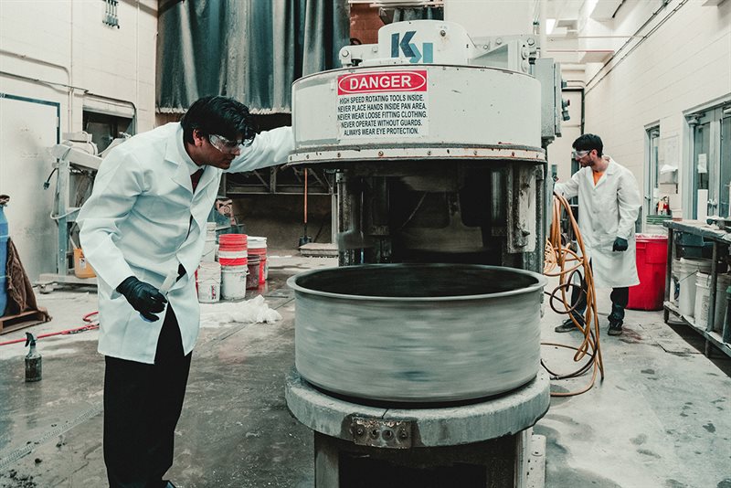 Man in lab coat looks inside a concrete mixing machine