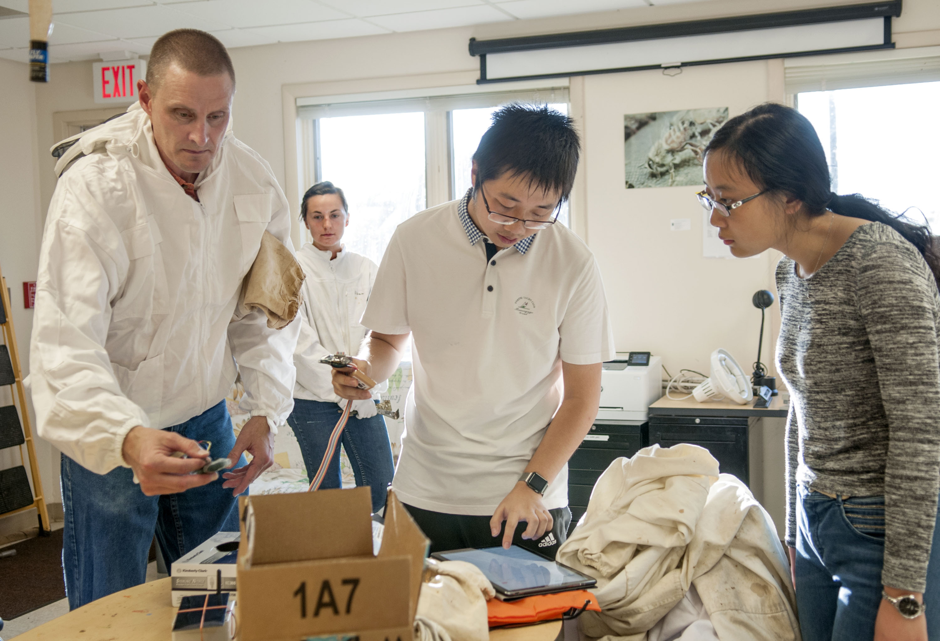 Jimmy He (center) checks the signal using a makeshift application to monitor a data stream, as WaggleNet team members, Chris Schmitz (far left) and Xiaolin Wu (far right) help to prepare deployment of the wireless monitoring system at the Bee Research Facility in Urbana. Beekeeper Ali Sankey (background left) is the lab manager and the team&amp;rsquo;s first client. The ECE students have been working on WaggleNet with Schmitz, their professor in ECE 110, since last fall. Schmitz, also a beekeeper, has shared his expertise on bees with He and Wu.