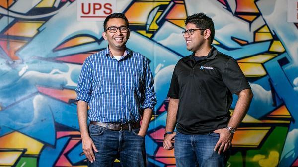 photo of two young men in casual dress in front of an art wall