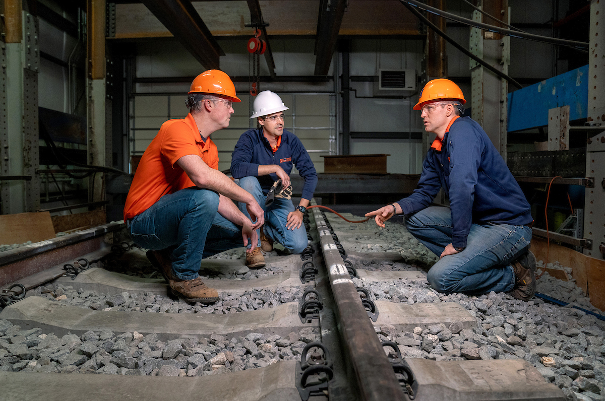 RailTEC faculty, J. Riley Edwards, assistant professor, left, Arthur de Oliveira Lima, research engineer, center, and Marcus Dersch, principal research engineer, right, gather at the full-scale track loading system at the Research and Innovation Laboratory (RAIL) in Champaign on April 11, 2024. The faculty are advancing the railroad engineering program while providing hands-on training to the next generation.