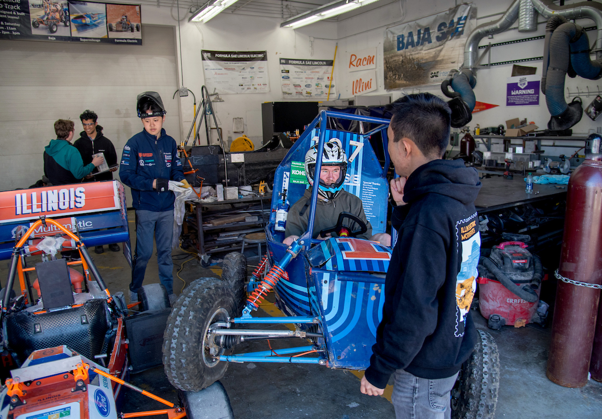 A student driving a racecar out of a garage while other students watch.