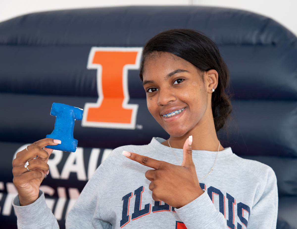 Smiling female in gray Illinois sweatshirt points to a Block I shaped cookie.